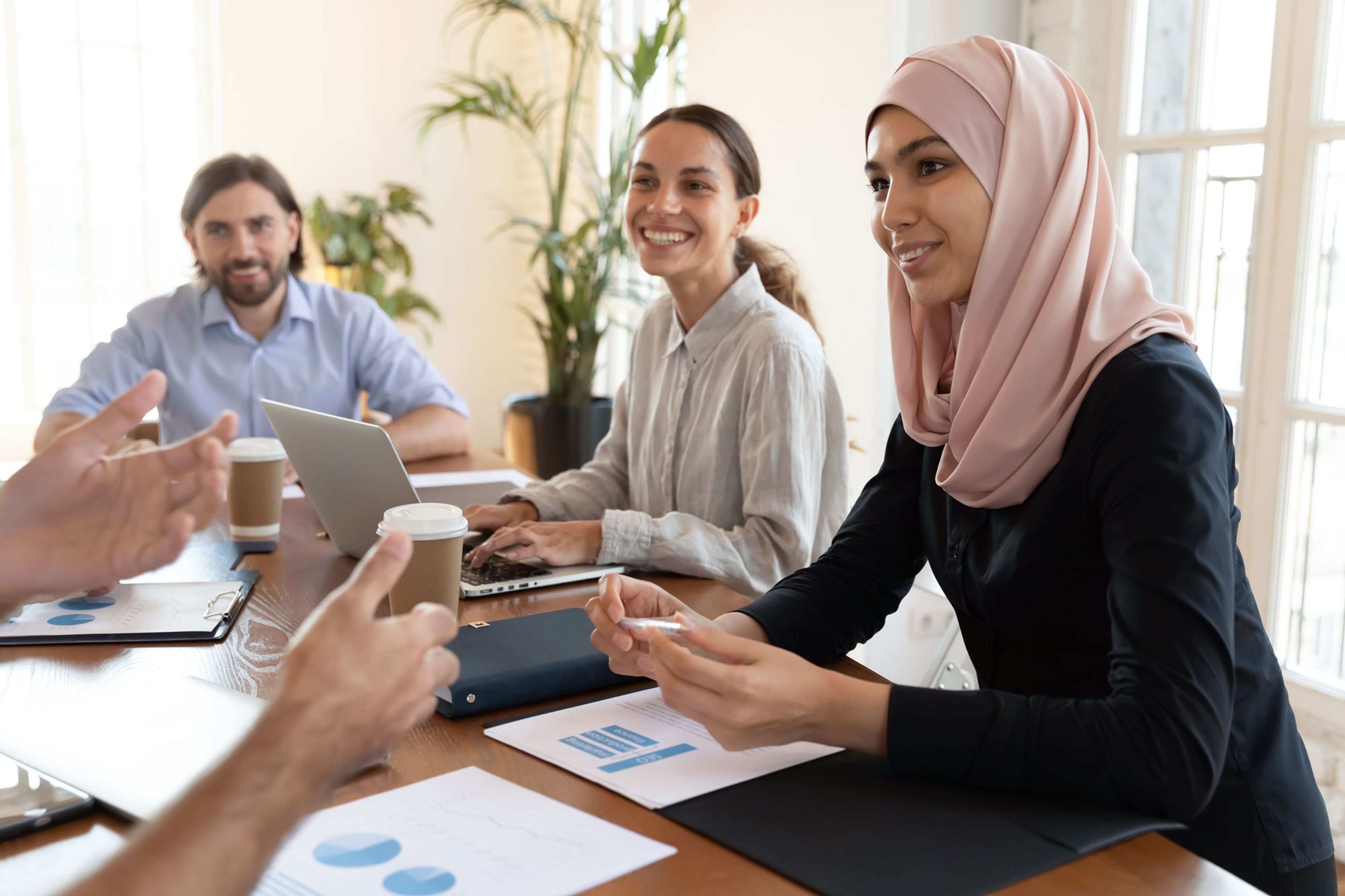 Flere personer i et møte rundt et bord, blant dem en kvinne med rosa hijab.