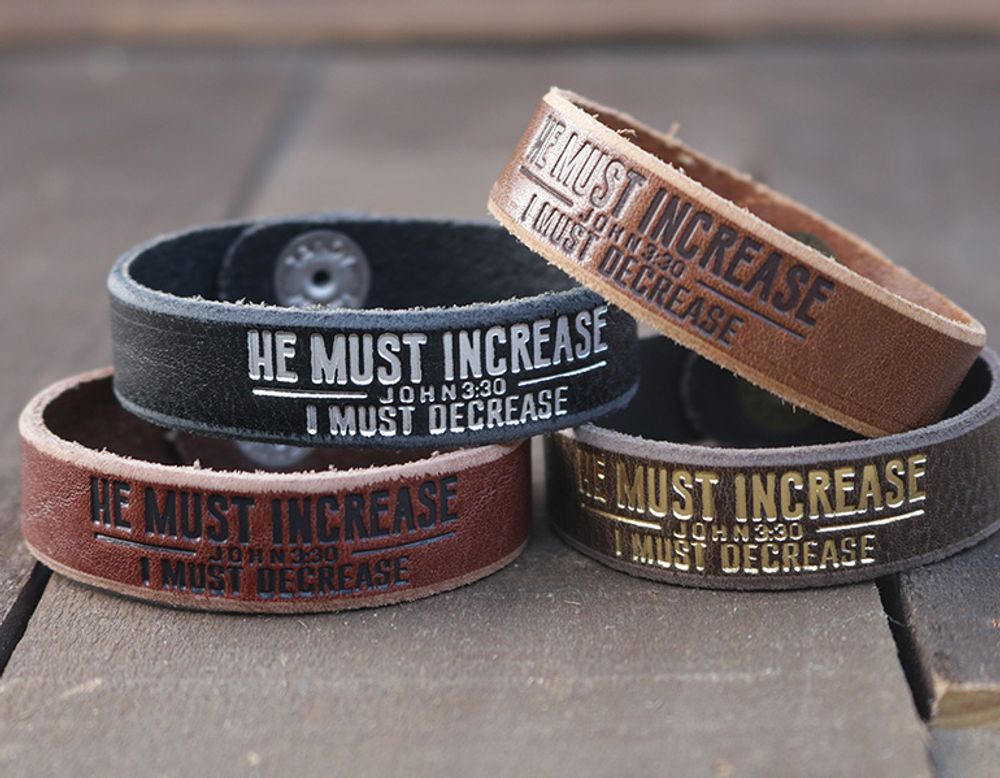 Stack of engraved leather cuff bracelets reading “He Must Increase, I Must Decrease, John 3:30” in assorted colors