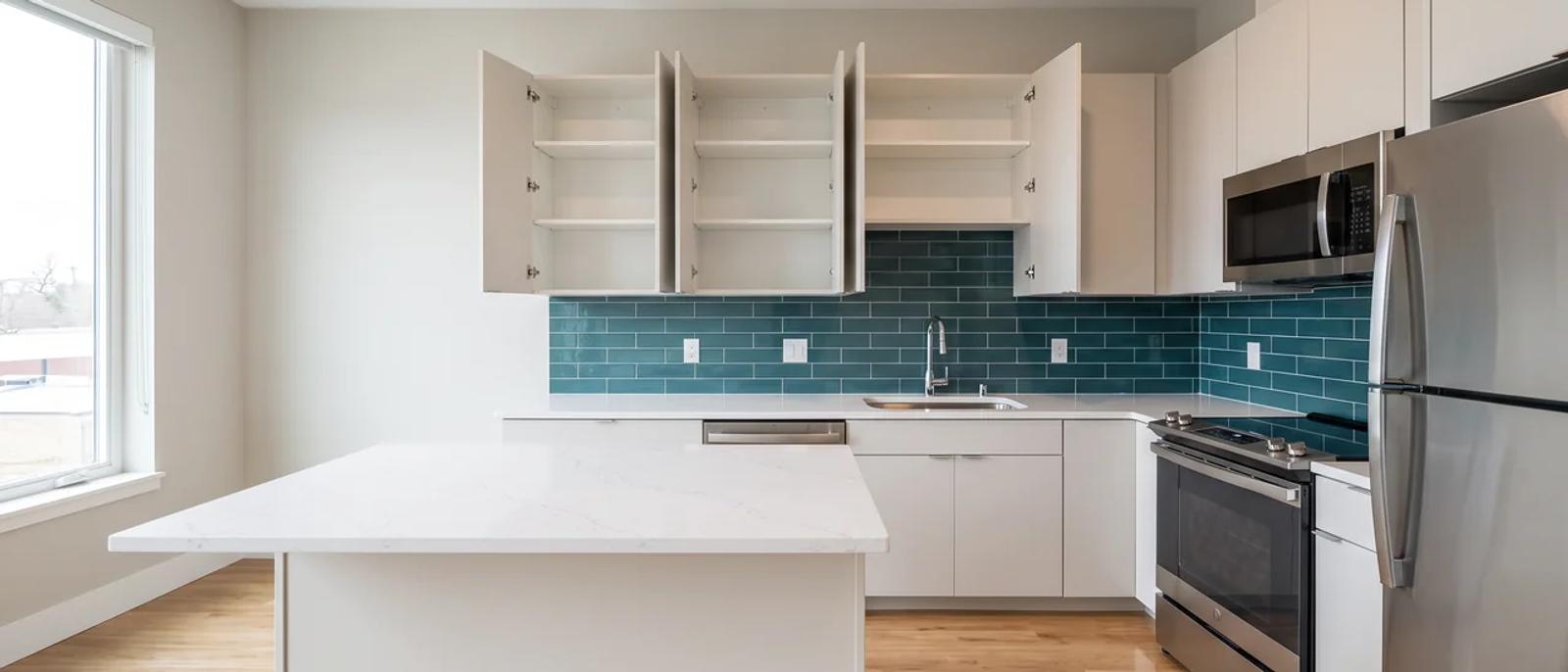 A clean, empty apartment kitchen with bare counters and open cabinets, ready for a new resident