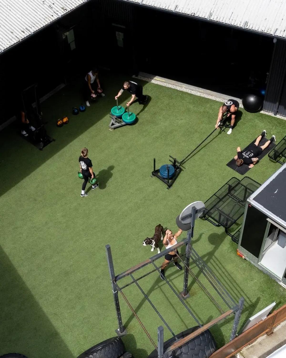 Outdoor training area with turf, sleds, and functional fitness equipment.