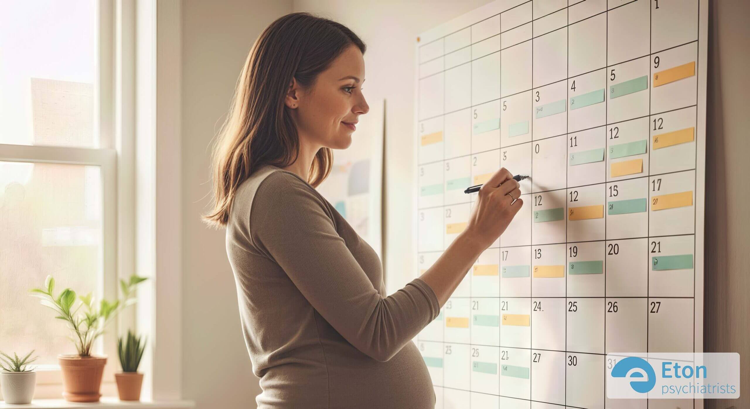A smiling pregnant woman writing on a large wall calendar, proactively organizing her schedule.