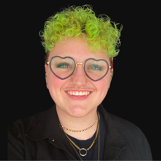 A headshot of Helena Buttons, who has green curly hair and heart glasses