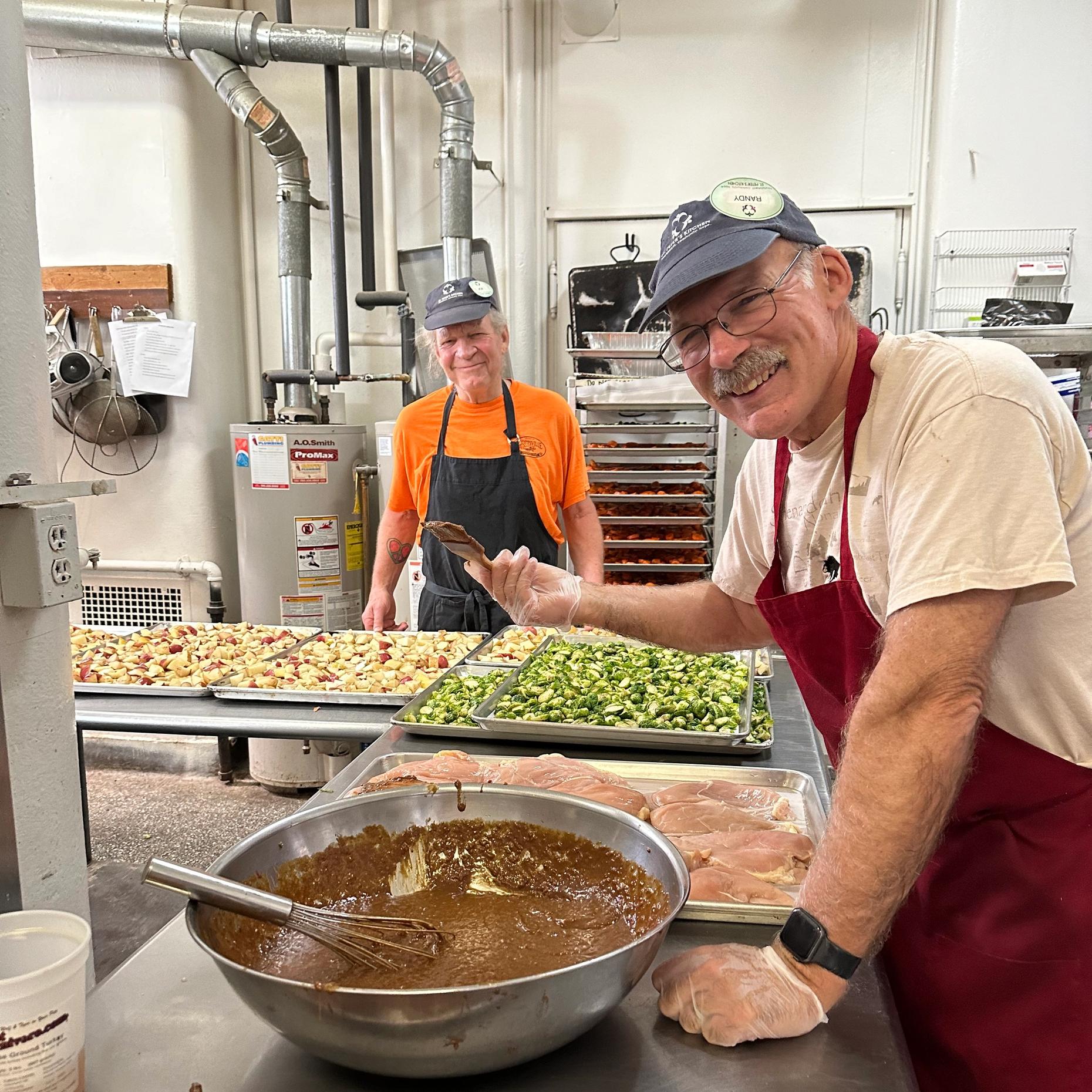 Volunteer cooks Joe and Randy prepare chicken and vegetables in the kitchen