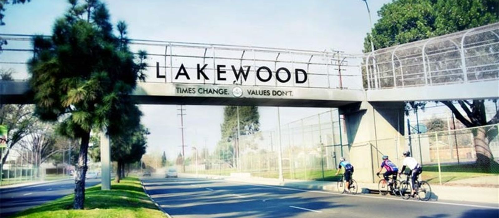 Lakewood city bridge sign reading "Times Change. Values Don't." with tree-lined boulevard and cyclists