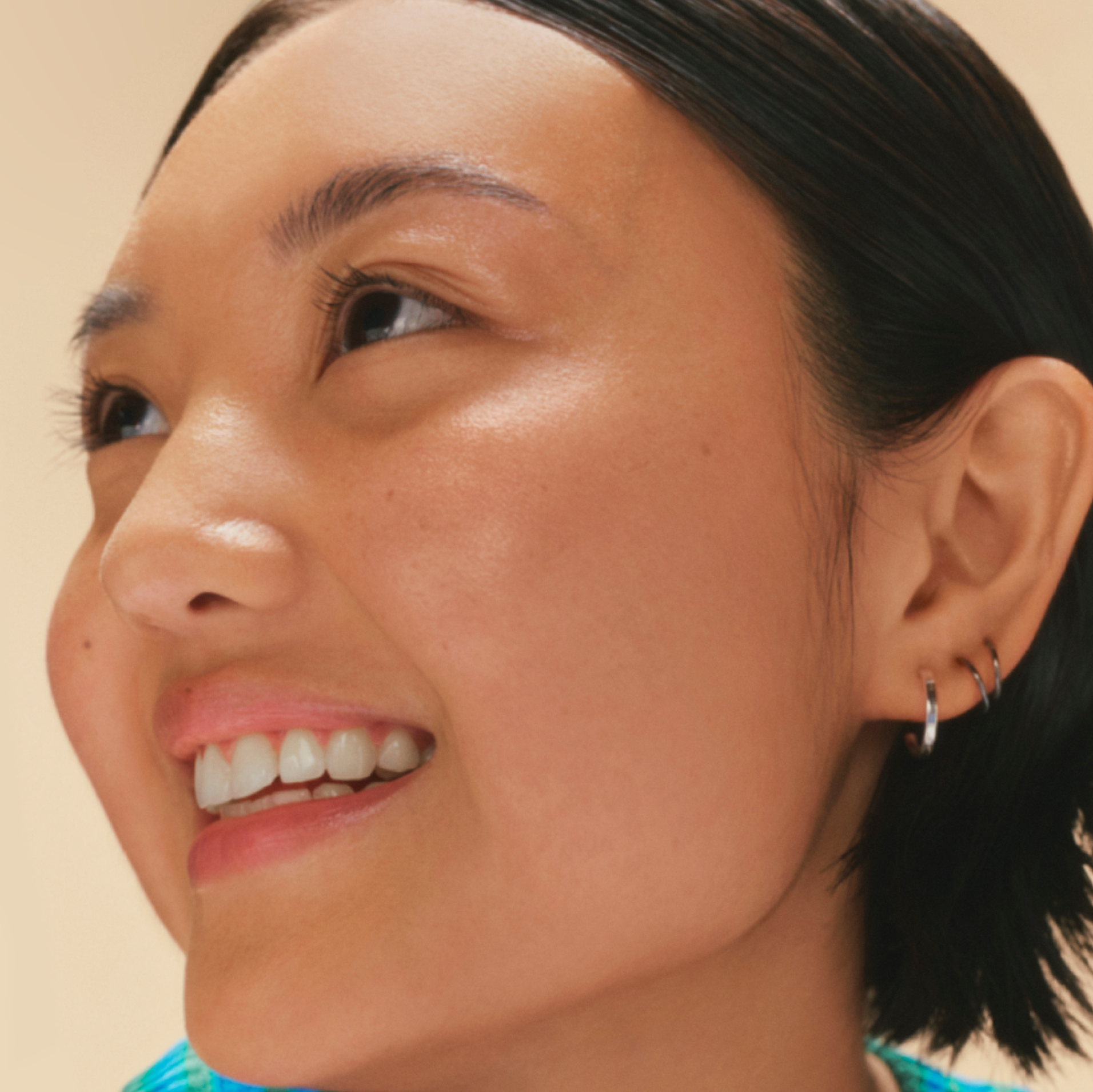 Close-up portrait of a smiling young woman, gazing upward on a warm beige background.