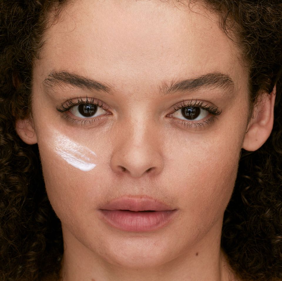 A closeup of a model with a swatch of eye cream under her left eye.