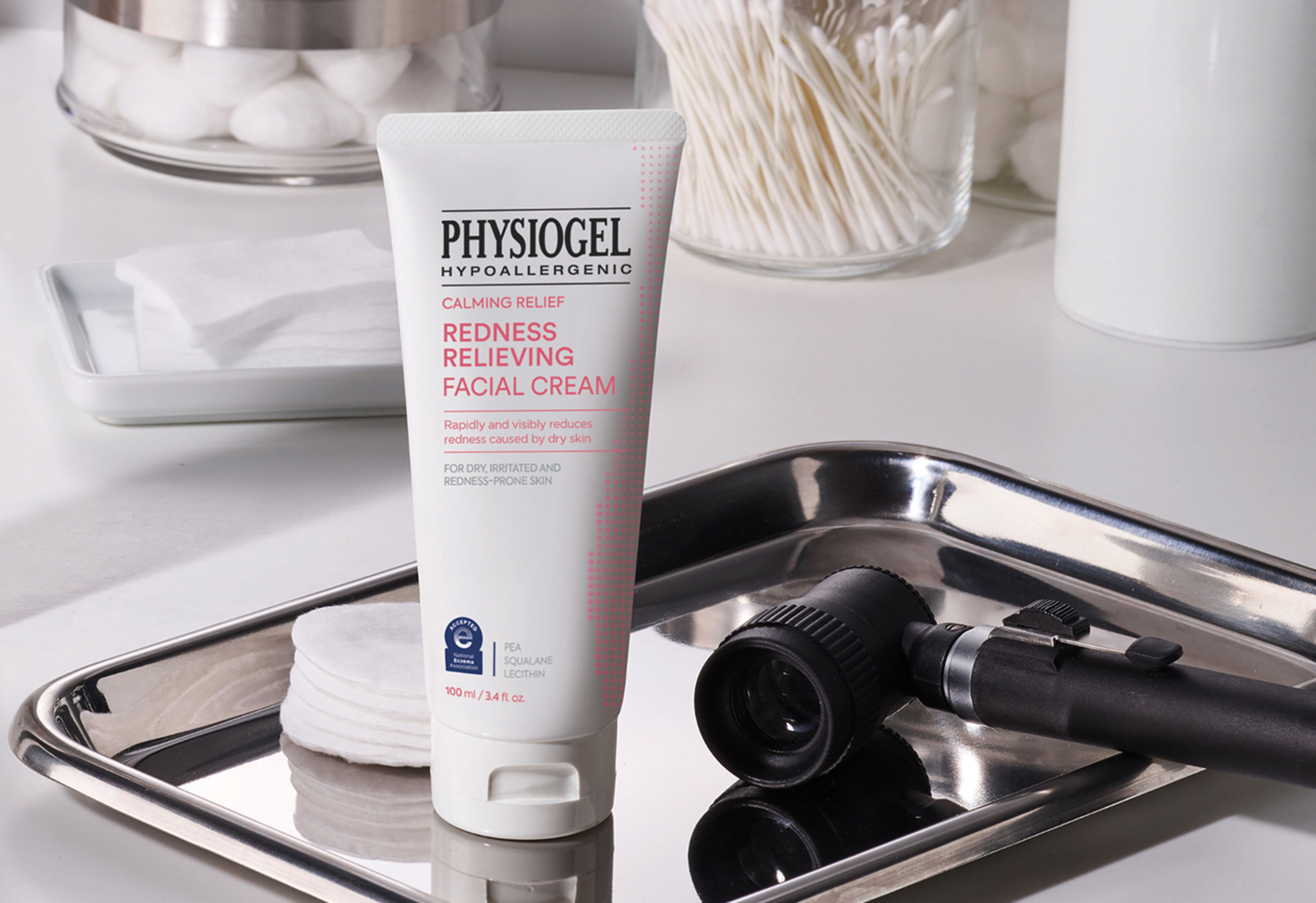 A tube of Physiogel Redness Relieving Facial Cream on a counter with cotton pads and a dermatoscope.