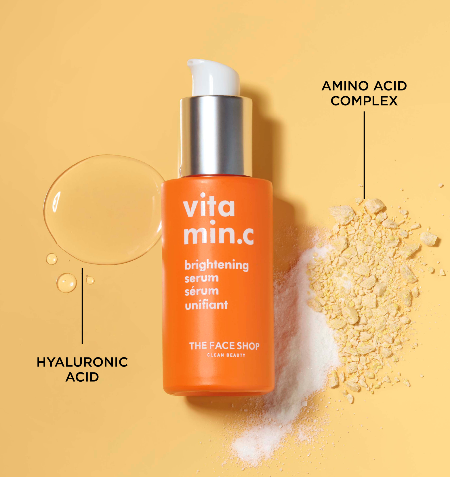 A small orange bottle of The Face Shop Vitamin C Skin Brightening Serum lying on a light orange surface with a drop of hyaluronic acid and a bit of amino aced complex powder