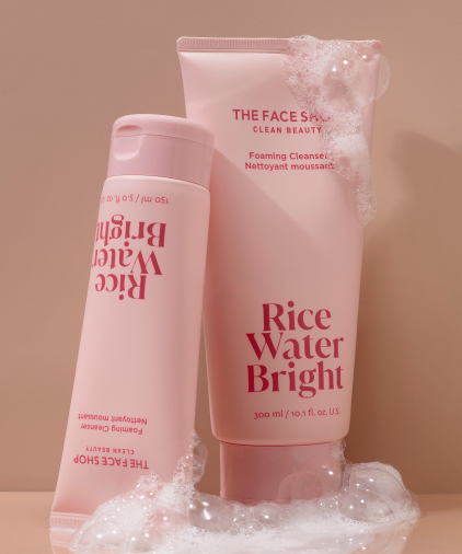 A closeup of of a 150 ml tube and a 300ml tube of Rice Water Bright Foaming Cleansers leaning on eachother, covered in bubbles