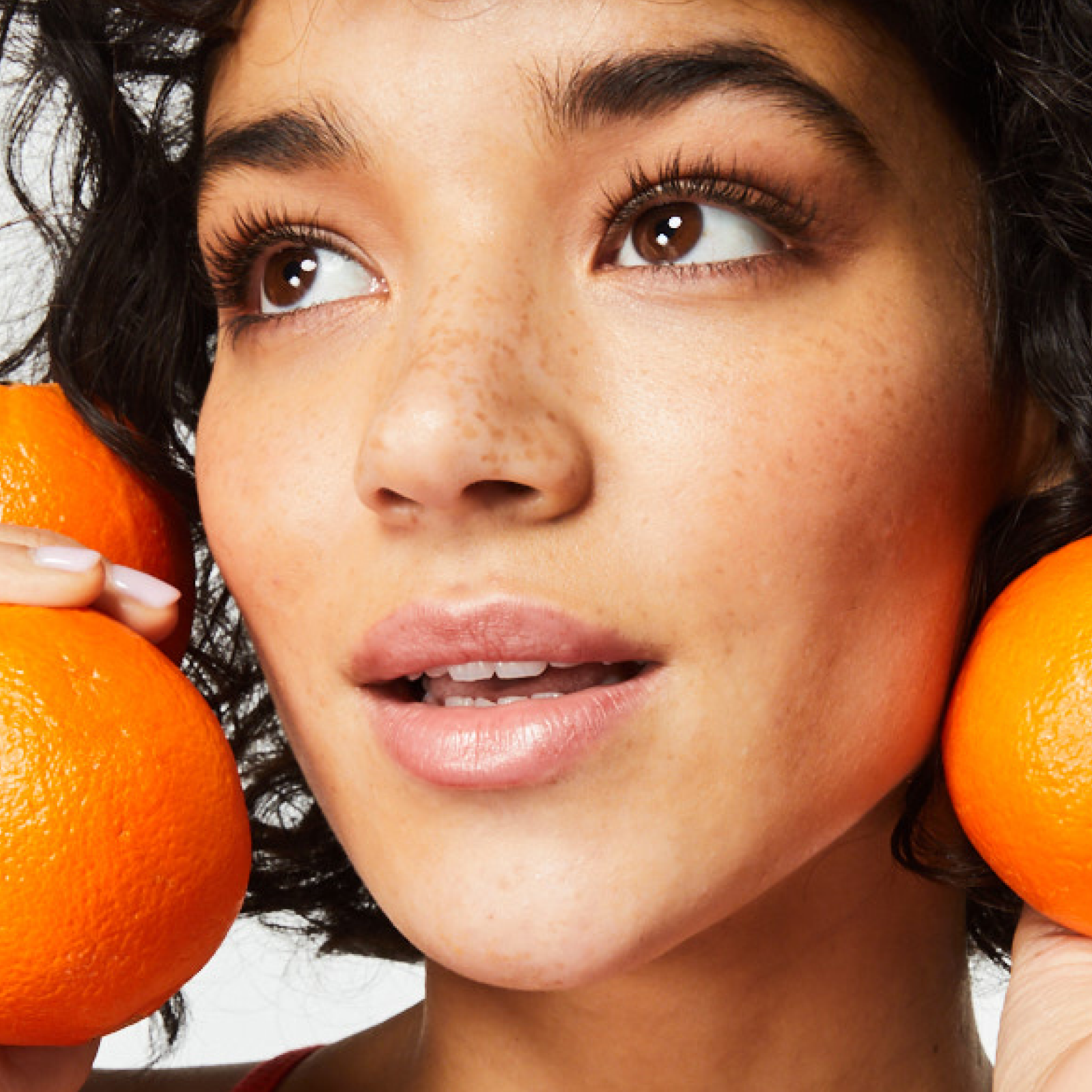 The woman's face with clear skin after using The Face Shop skin care products. The woman is holding oranges next to her face demonstrating the effects of the Vitamin C.