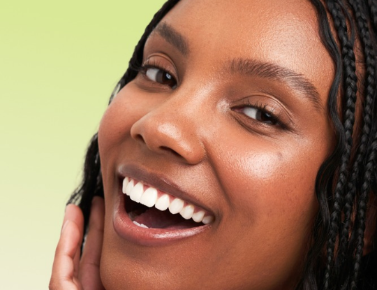 Smiling Black woman with braided hair and radiant skin.