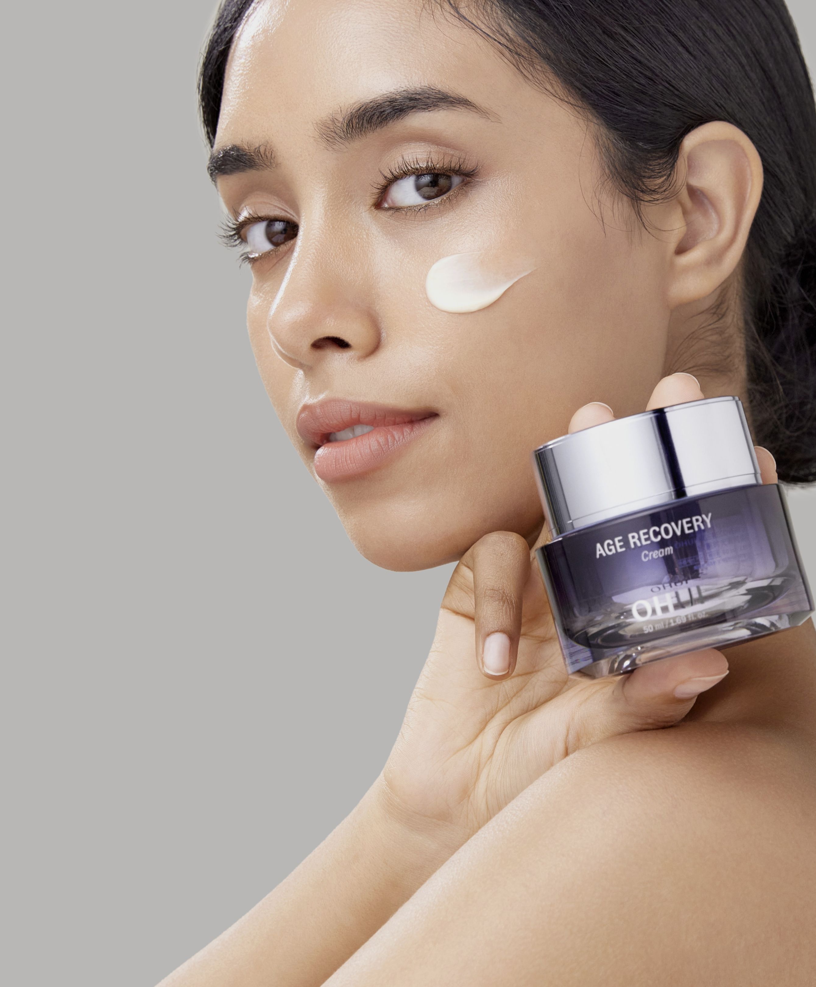 Split image of a model holding OHUI Age Recovery Cream over her shoulder and editorial image of  Reverse Activator Cream next to a texture swatch on a white background..