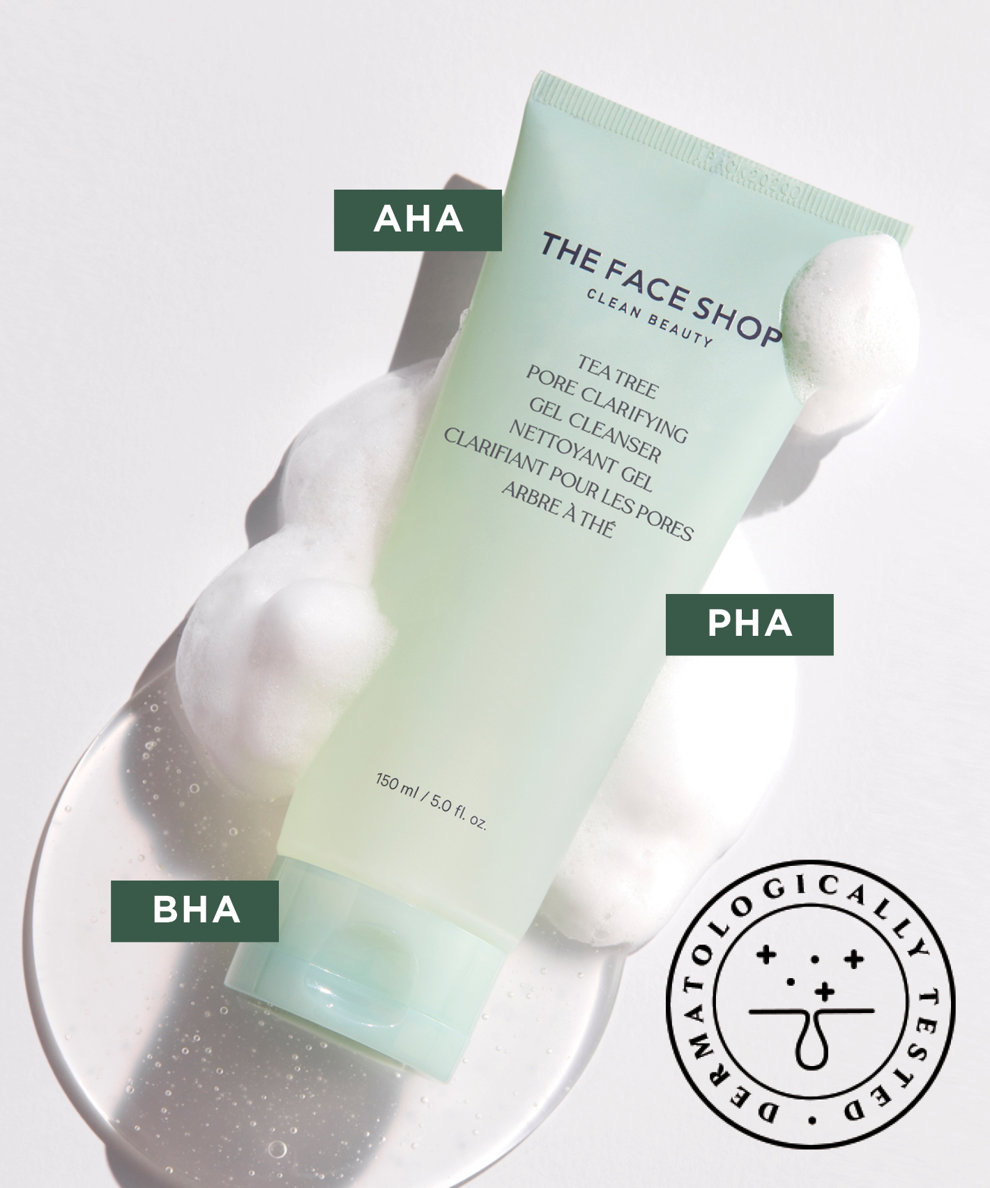 A light green tube of The Face Shop Tea Tree Pore Clarifying Gel Cleanser lying in a tiny puddle of liquid and foam on a white surface. Three abbreviations are attached to the image: AHA, PHA, BHA and also a stamp saying "Dermatologically Tested"
