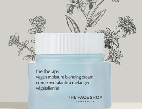 A light blue jar of THE FACE SHOP vegan moisture blending cream with a white lid, against a background of botanical illustrations.