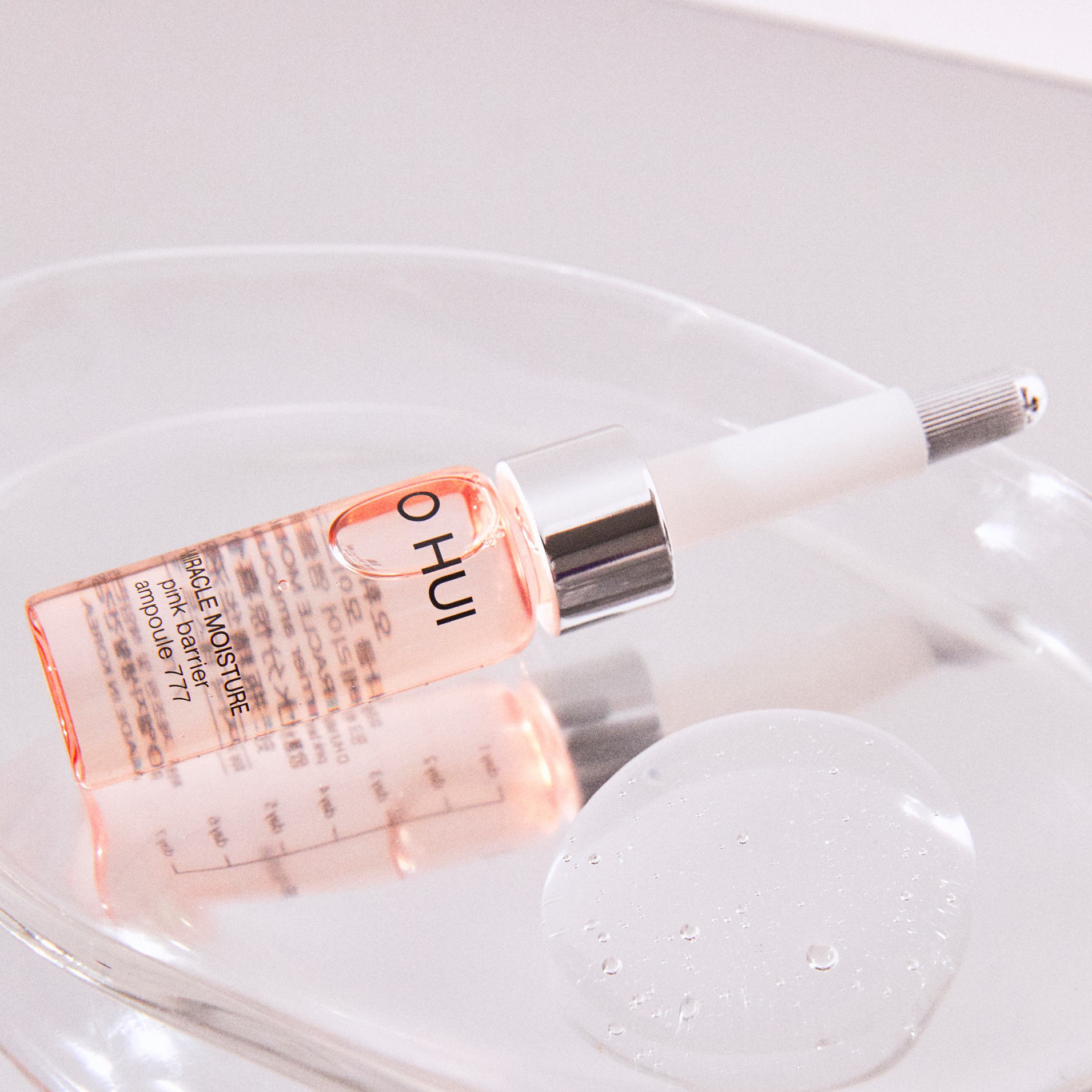 A bottle of OHUI Miracle Moisture 777 Serum on a surface with a drop of texture next to it on a surface.