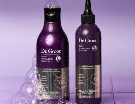 Two purple Dr. Groot scalp revitalizing solution bottles, one a shampoo with bubbles and one a treatment bottle with water droplets.