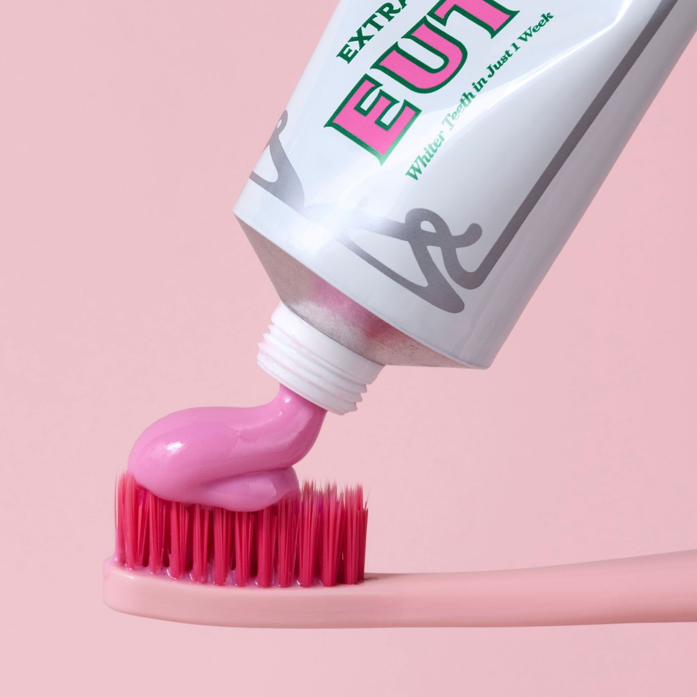 Pink Euthymol Whitening Toothpaste squeezed from a white tube onto a pink Euthymol Toothbrush.