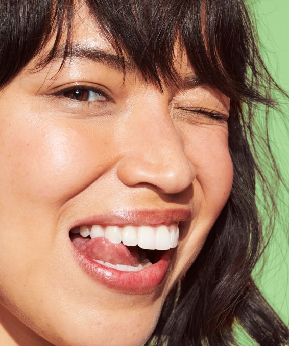 A model smiling and winking at the viewer, showing her teeth perfectly white and clean and shiny after using Reach POP Whitening Peppermint Twist Dental Floss
