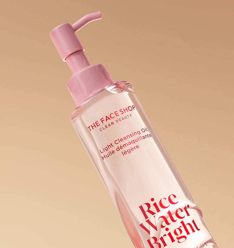 A bottle of The Face Shop Rice Water Bright Light Cleansing Oil drenched in oil on a warm beige background