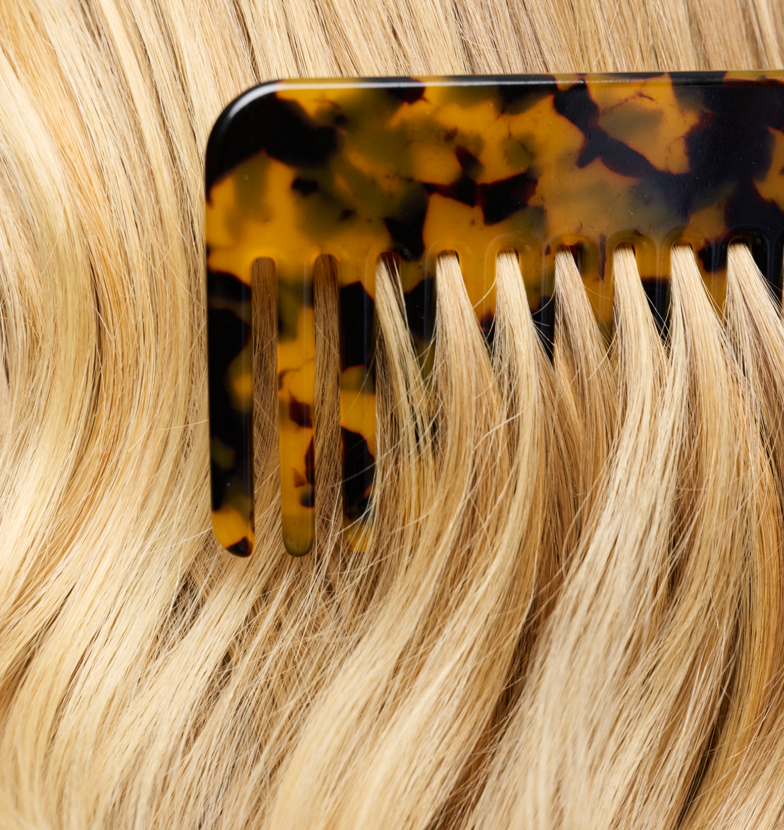 A close up of a comb running through healthy and shiny blonde hair.