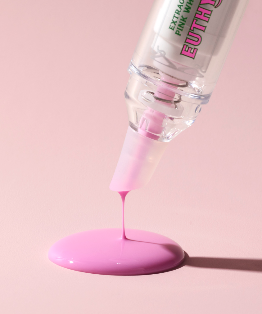 A tiny pink puddle dripping out of transparent tube of Euthymol whitening gel on a pink surface