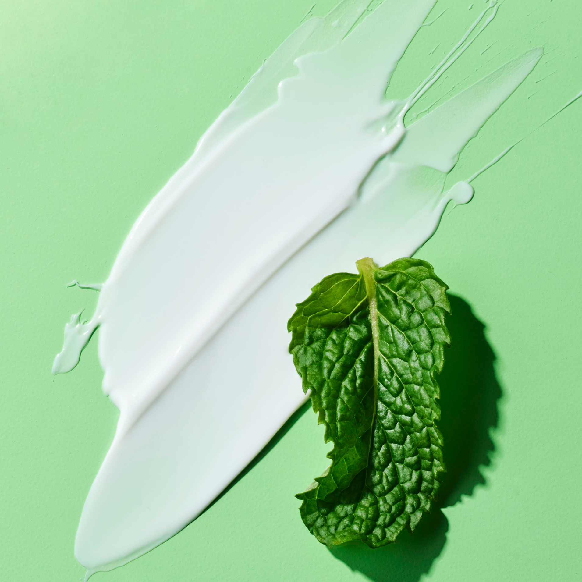 A white spread of POP Mint Toothpaste on a green surface with a mint leaf on it.
