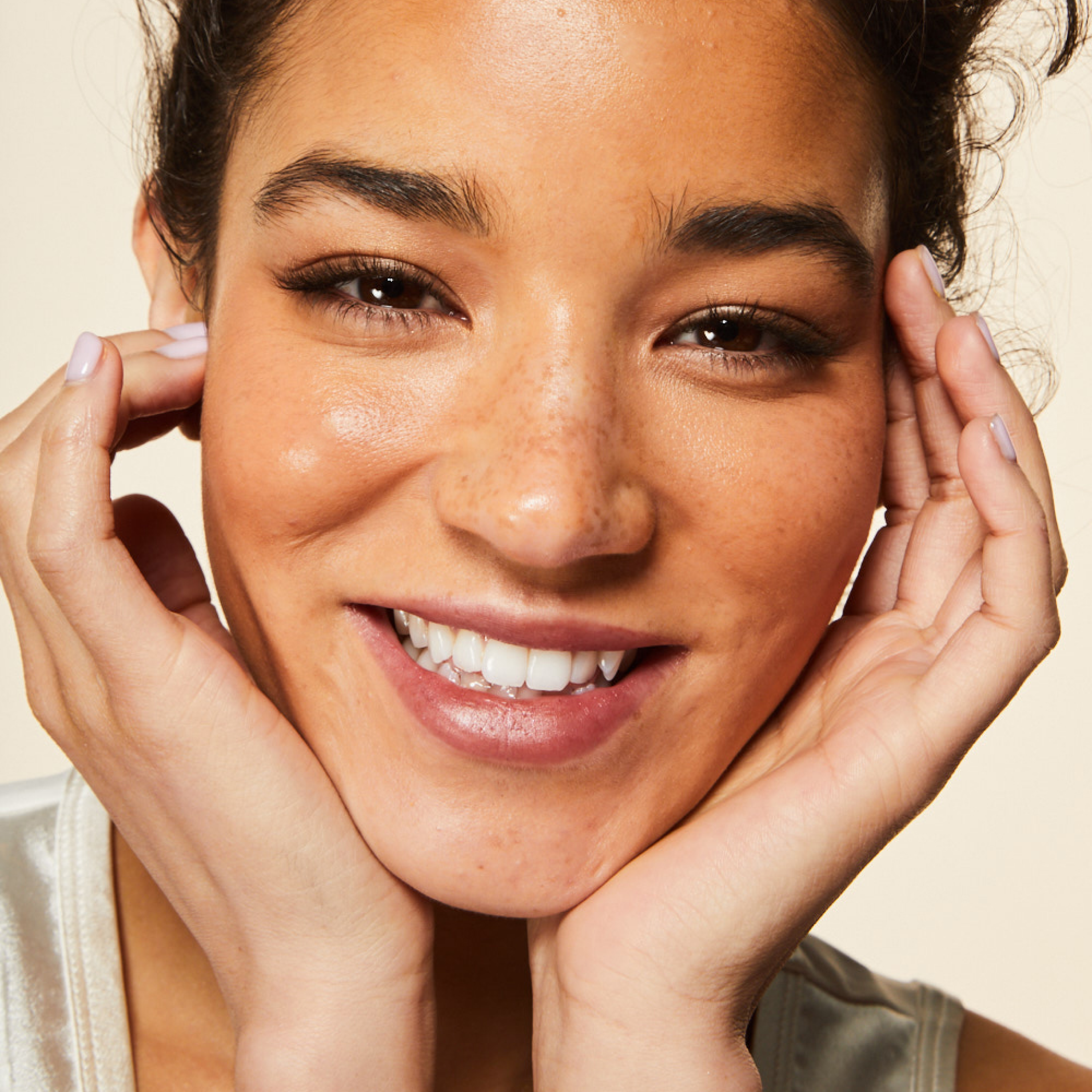 A model smiling touching her face and neck with her hands, looking right at the viewer