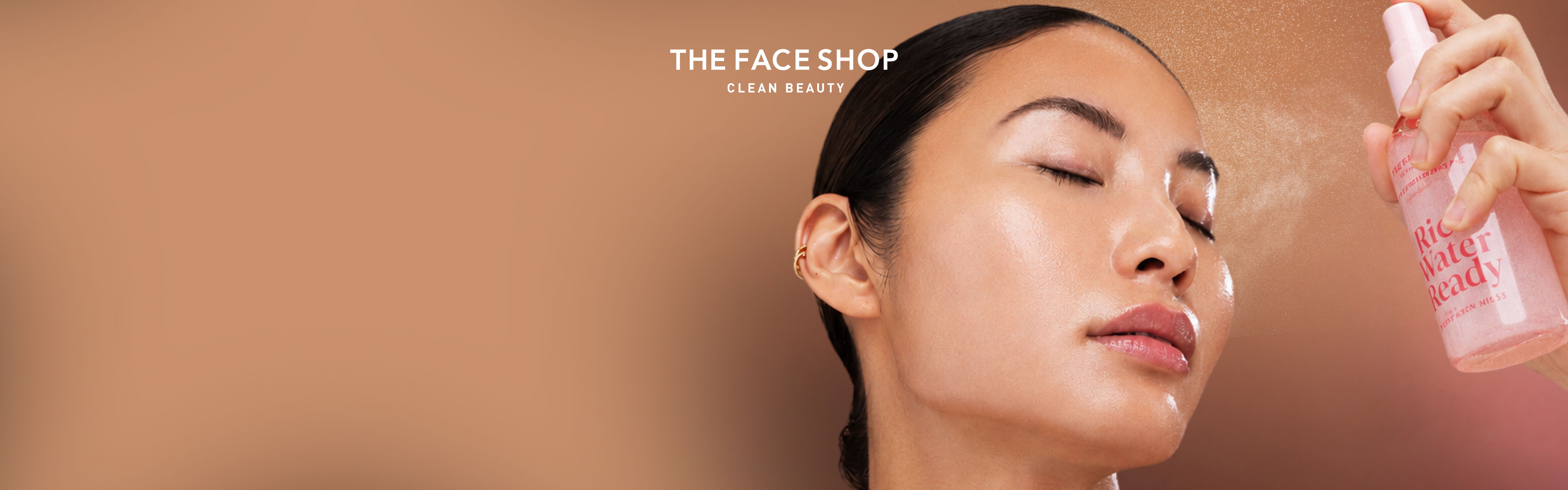 A woman with glowing skin closes her eyes as she is sprayed with a pink face mist from 'The Face Shop'.