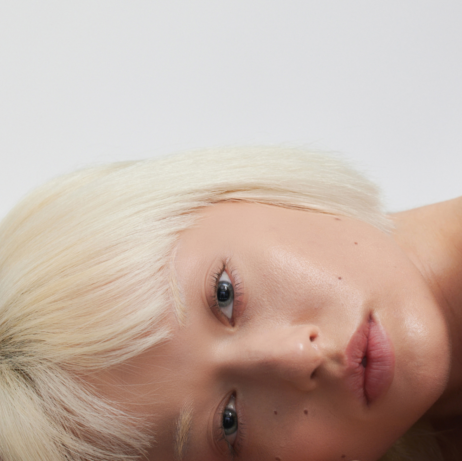 A close-up of a woman with blonde hair and bangs lying on her stomach, head tilted to the side, in a relaxed position.