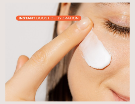 Close-up of a person's finger applying a white cream to their cheek, with text "INSTANT BOOST OF HYDRATION."