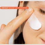 Close-up of a person's finger applying a white cream to their cheek, with text "INSTANT BOOST OF HYDRATION."
