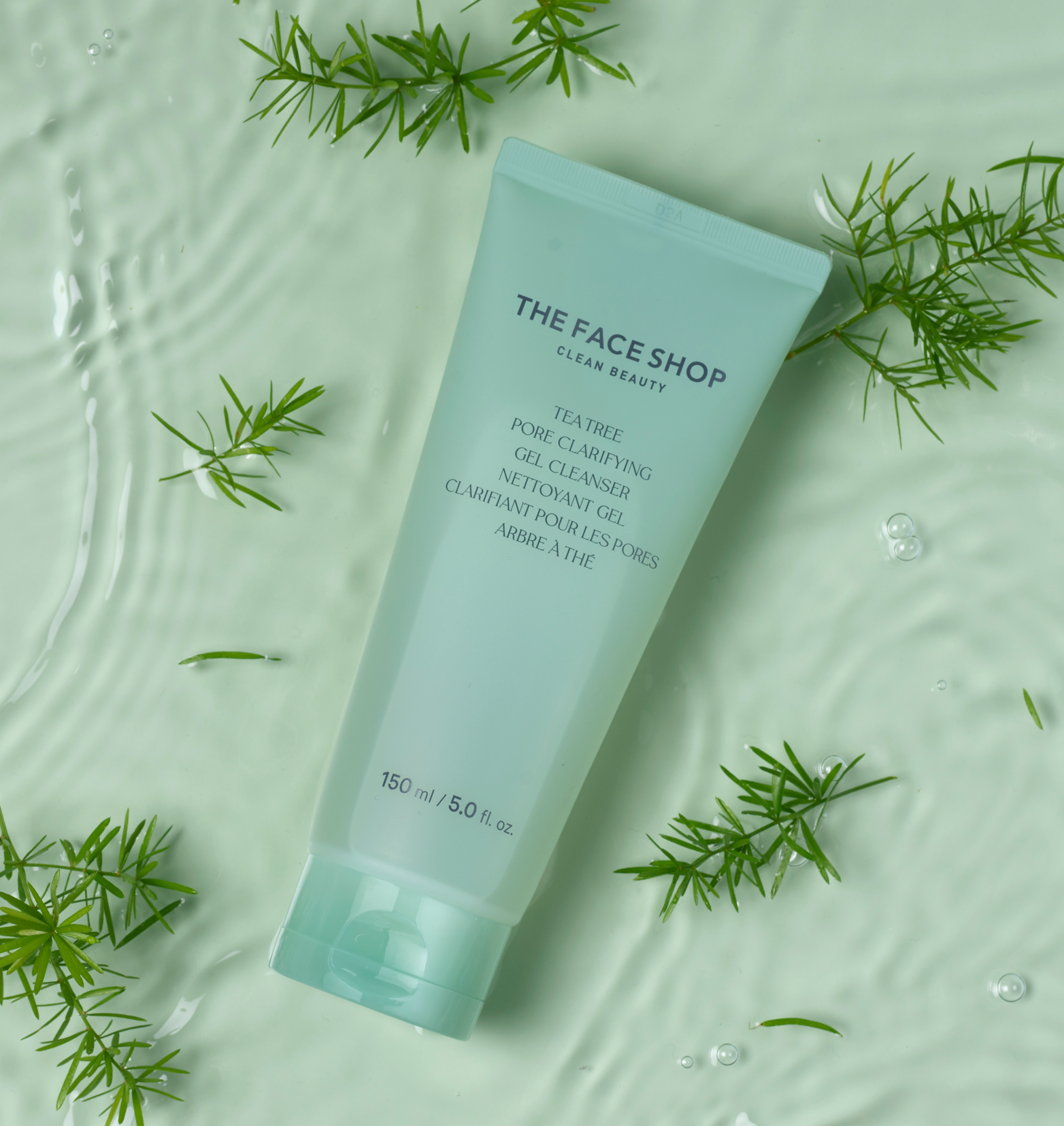 A light green tube of The Face Shop Tea Tree Pore Clarifying Gel Cleanser over a light green liquid surface with green Tea Tree twigs scattered around