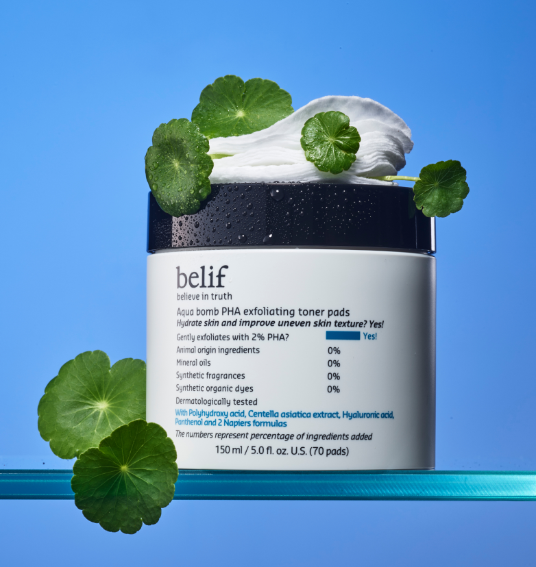 A container of belif Aqua Bomb PHA Exfoliating Toner Pads sits on a glass helf with natural herbs and toners pads resting on top of it