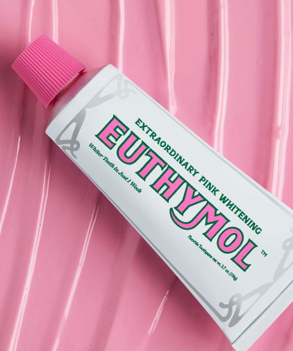 An image of Euthymol Original Toothpaste tube over a blanket of pink toothpaste texture.