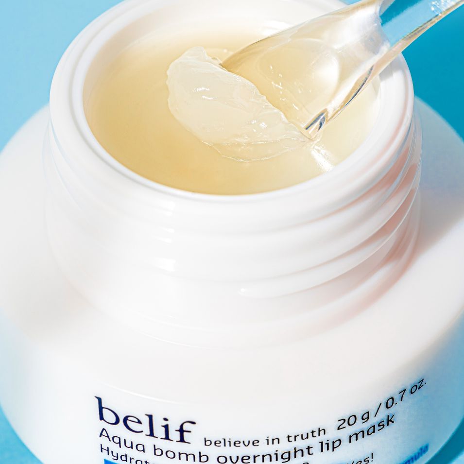 A white jar of belif Aqua Bomb Overnight Lip Mask with no lid showing the texture of the mask being picked with a small spoon
