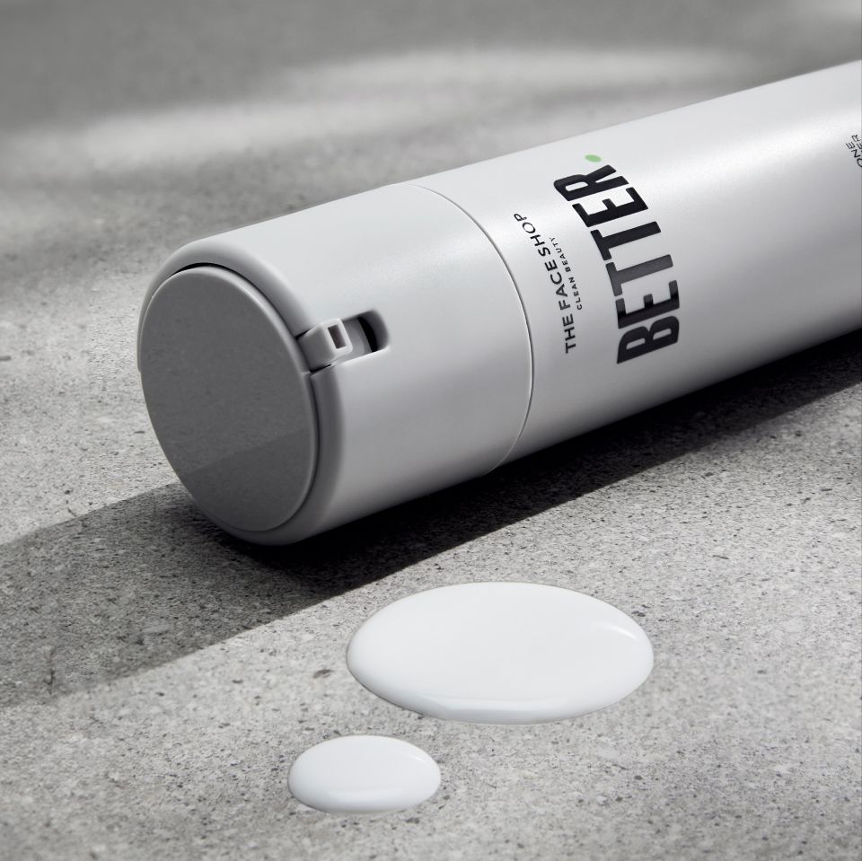 A white cylindrical bottle of BETTER lies on its side on a gray surface. The bottle has a small circular cap and a spout. Two dollops of white liquid are spilt next to it. .