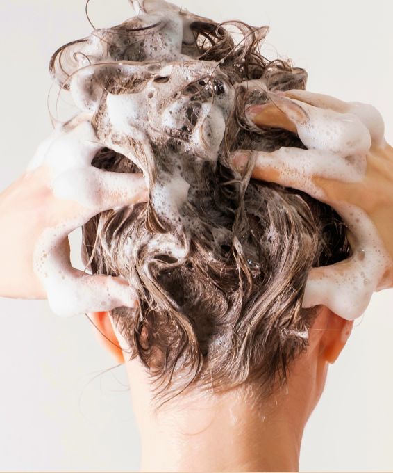 Hands lathering shampoo into wet, foamy hair.