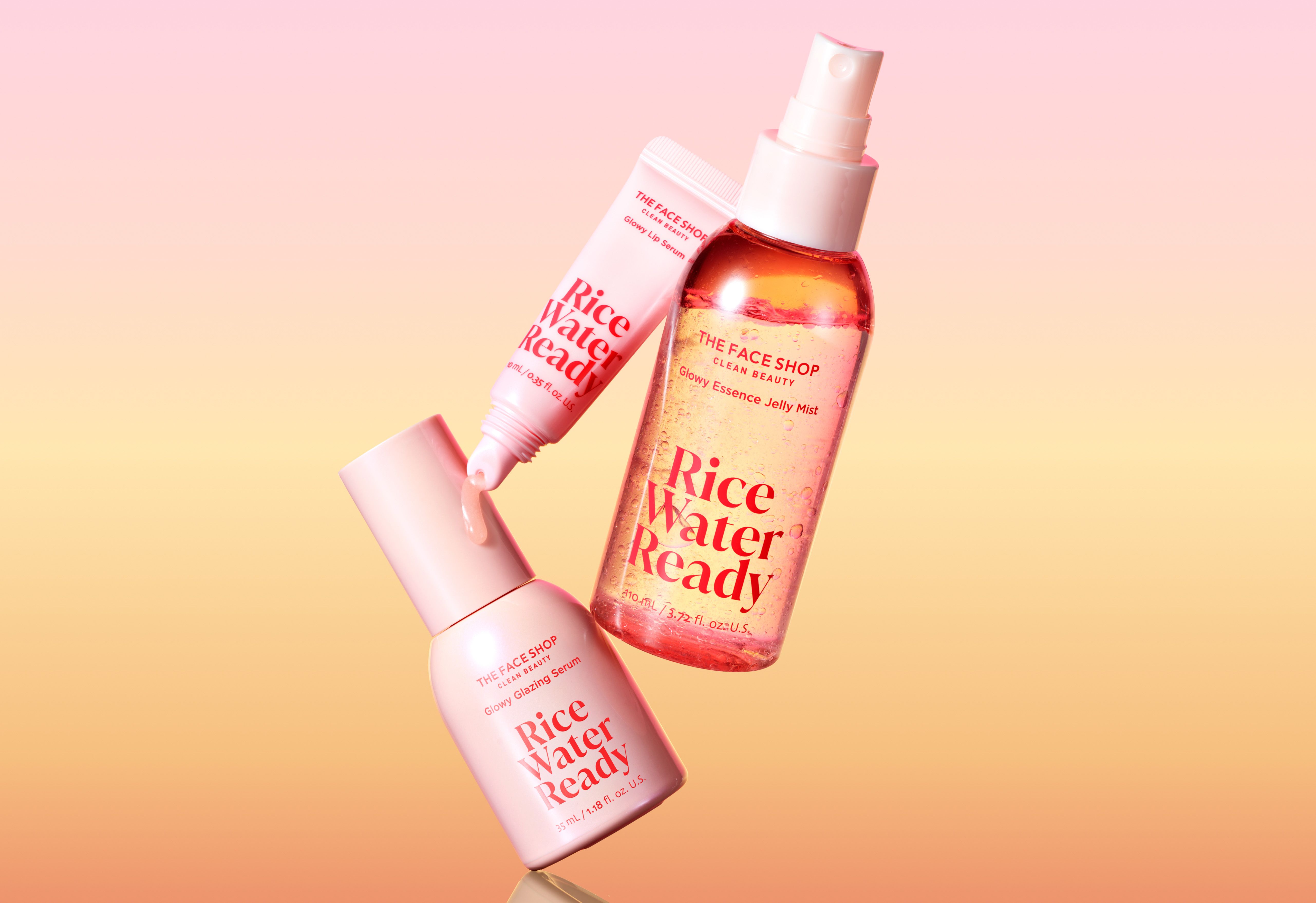 Three pink and clear "THE FACE SHOP Rice Water Ready" skincare products: a lip serum, a face serum, and a mist, on a pink and orange gradient background.