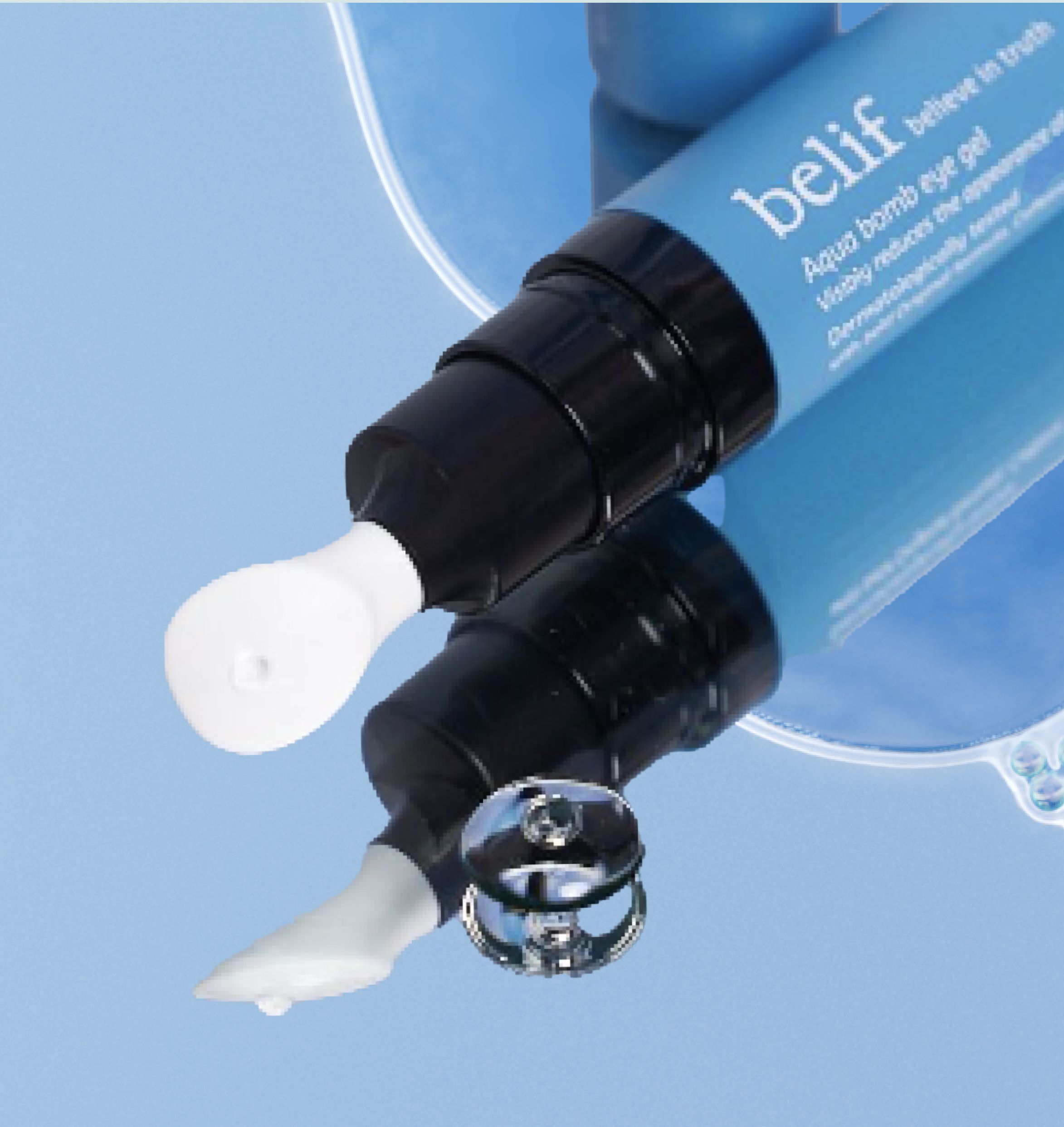 A tube of Belif Aqua Bomb eye cream is placed on a reflective surface next to its removed cap. The blue tube shows the product partially. A small amount of the cream is visible next to the tube.