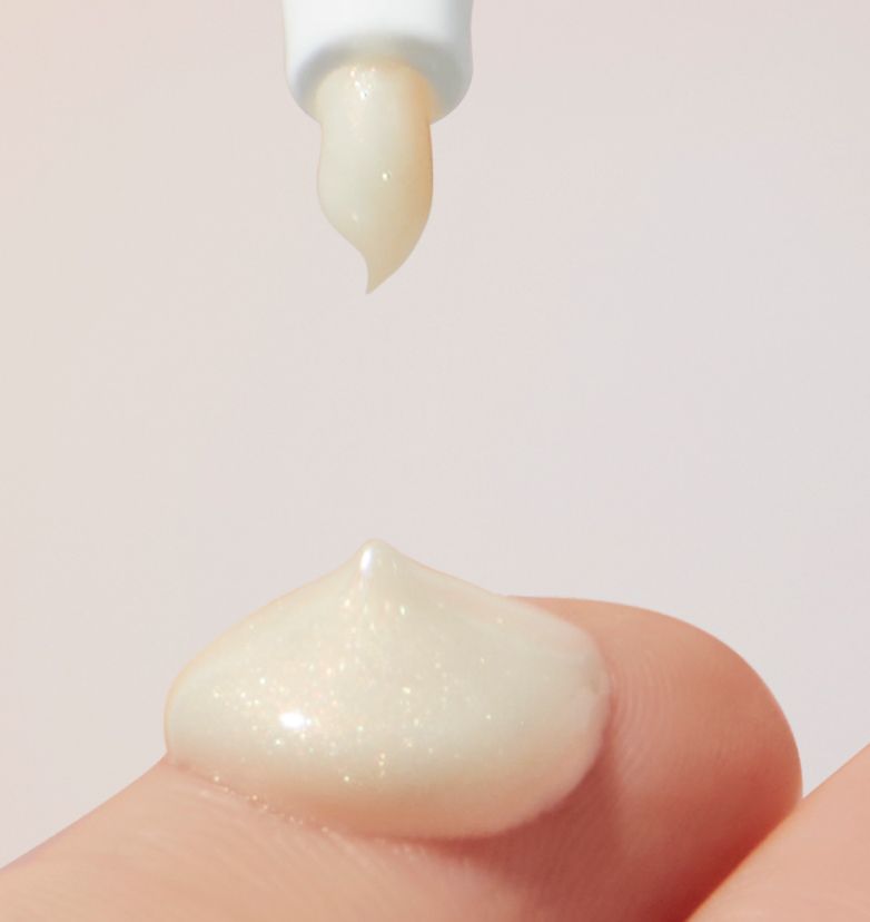 A closeup of belif Glow Serum being squeezed out of the nozzle held over a fingertip with a dollop of product on it.