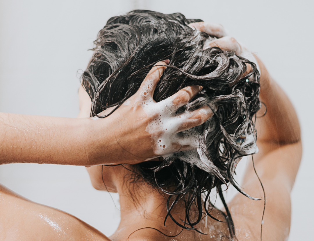 Person washing dark hair, hands covered in shampoo lather.