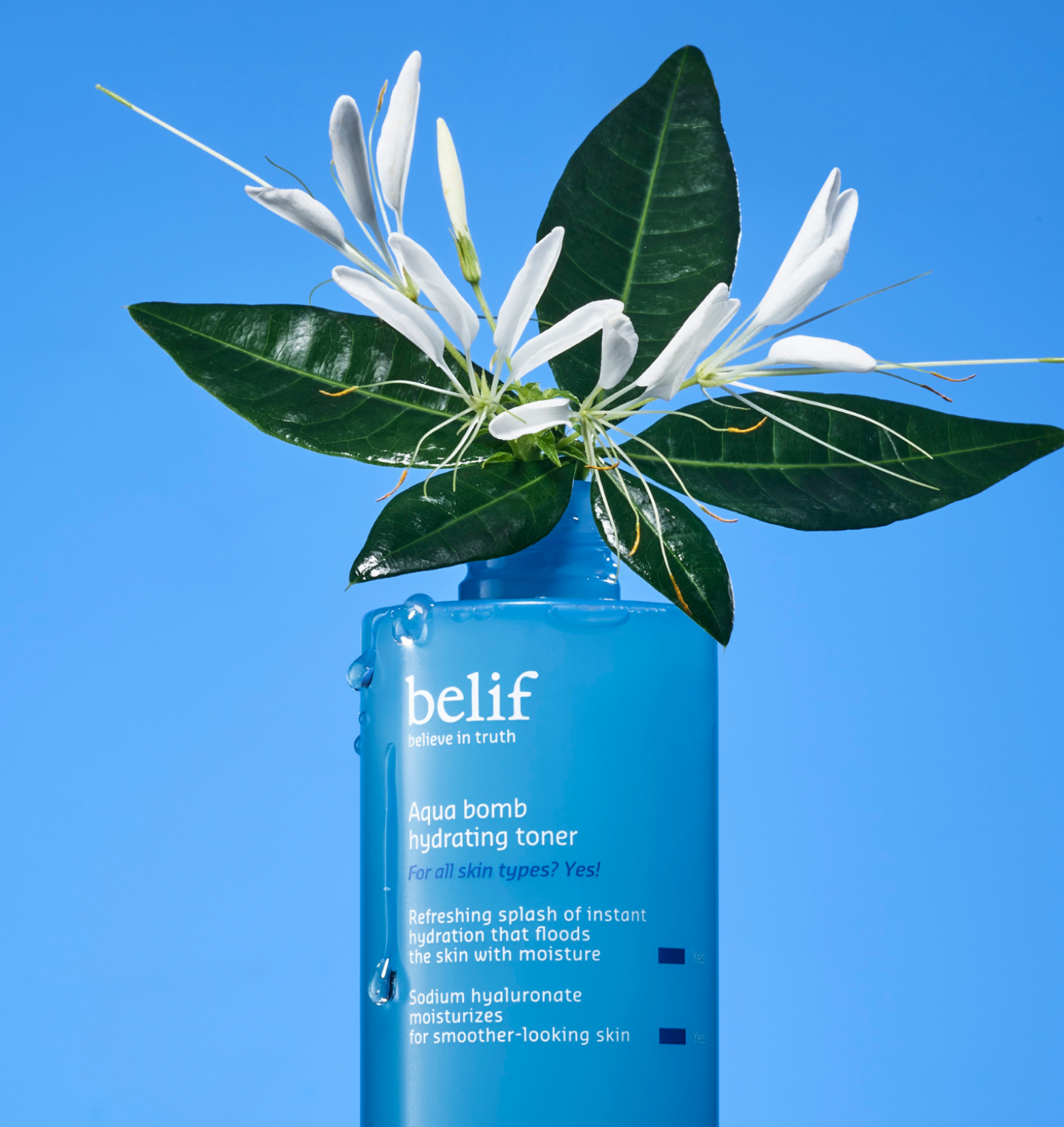 An open bottle of belif Aqua Bomb Hydrating Toner with a honeysuckle twig in it