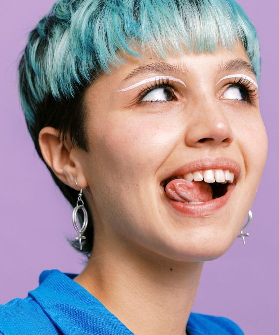 A model with light blue hair looking aside and smiling, showing her teeth perfectly white and clean and shiny after using Reach POP Cinnamon Dental Floss