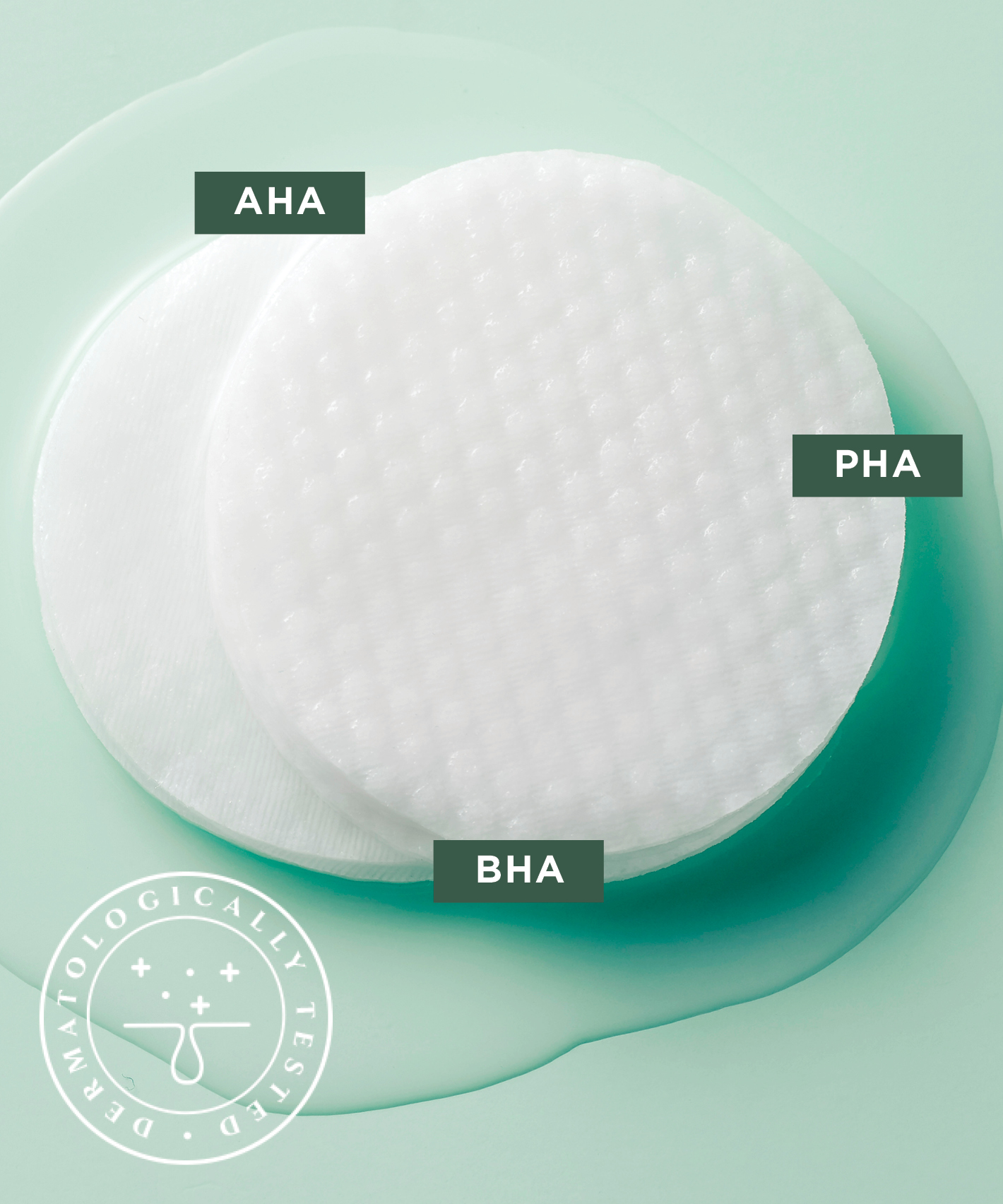 Two The Face Shop Toner Pads lying in a tiny puddle of liquid on a light green surface. Three abbreviations are attached to the image: AHA, PHA, BHA and also a stamp saying "Dermatologically Tested"