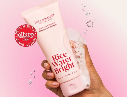 Pink tube of THE FACE SHOP Rice Water Bright Foaming Cleanser, an Allure Best of Beauty Award 2026 winner, held by a hand with foam.