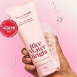 Pink tube of THE FACE SHOP Rice Water Bright Foaming Cleanser, an Allure Best of Beauty Award 2026 winner, held by a hand with foam.