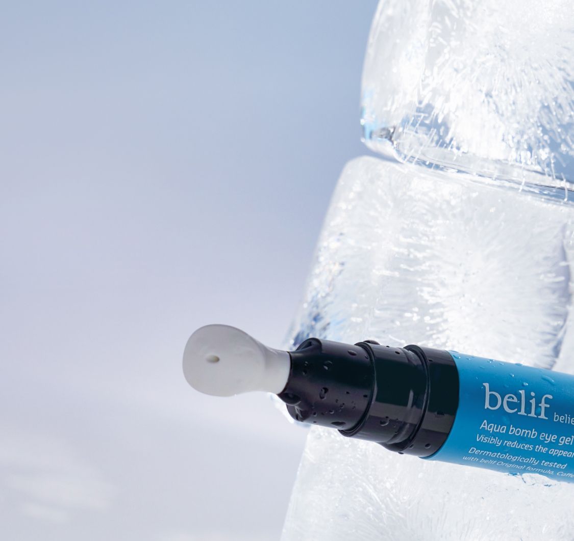 A tube of belif Aqua Bomb Eye Gel is positioned against an ice block background. The product name and description are visible on the blue tube.