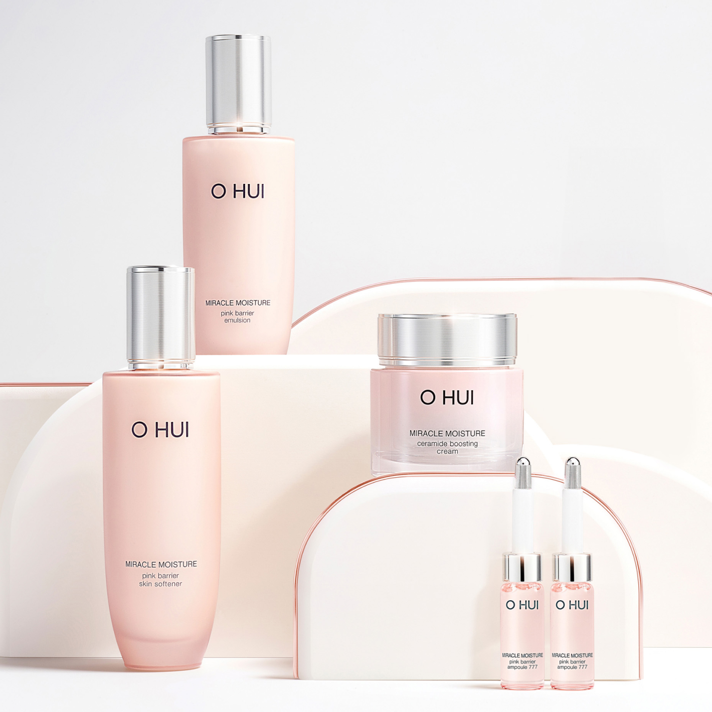 A display of OHUI Miracle Moisture skin care products, including pink bottles and jars of varied sizes, neatly arranged against a white and soft pink background.