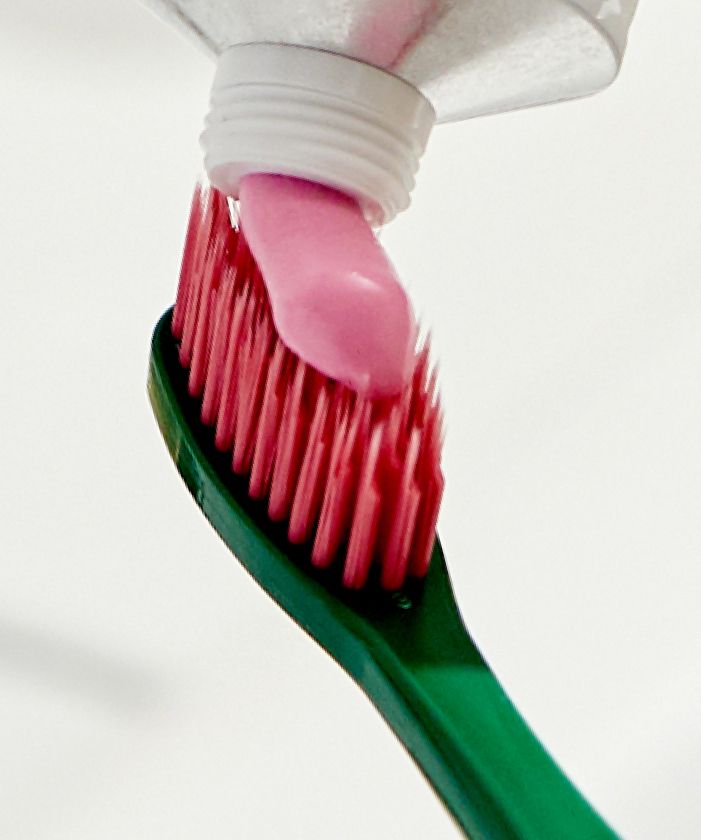 A close-up of a green Euthymol Original Regular Toothbrush with dark pink bristles, as Euthymol Toothpaste is being squeezed onto it from a tube.