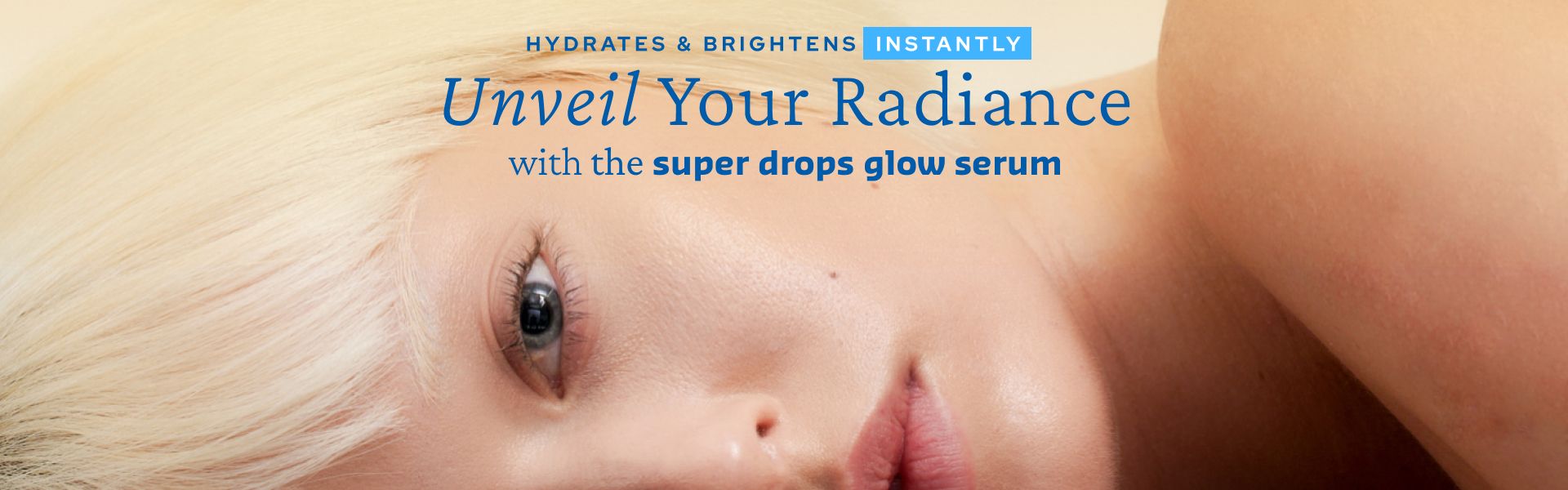 Close-up of a woman with short, blonde hair lying down with a visible eye and cheek. Text overlay reads: "Hydrates & Brightens Instantly. Unveil Your Radiance with the super drops glow serum.